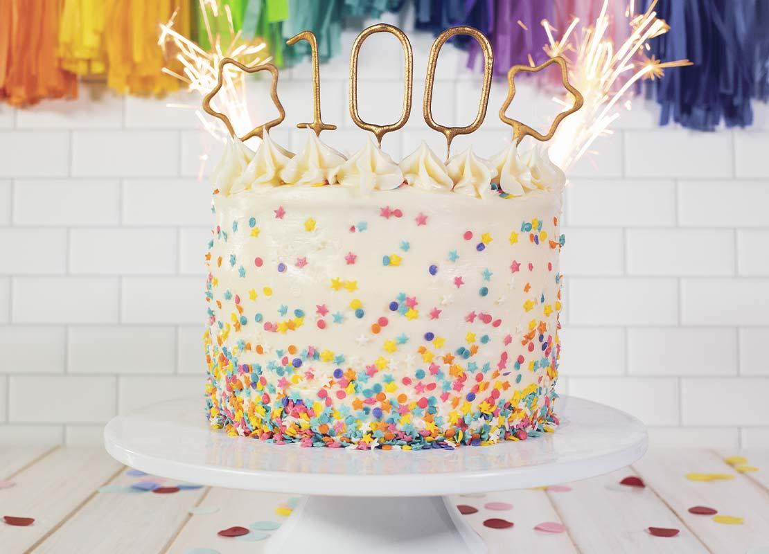 Pastel decorado con sprinklesm, velas tipo bengala y topper con el número 100