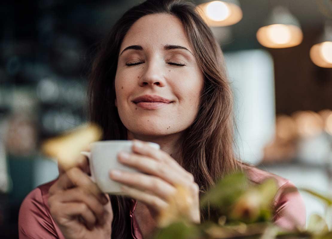 Mujer sostiene una taza de café frente a ella mientras disfruta de su aroma en una cafetería