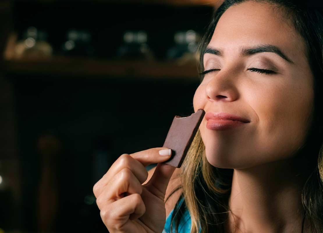 Con los ojos cerrados, mujer sostiene una tableta de chocolate frente a su rostro, disfrutando de su olor