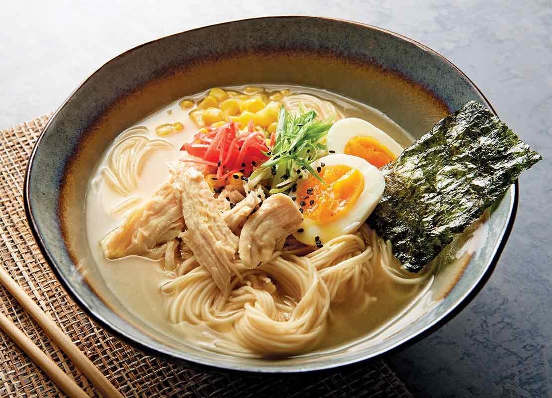 Plato de ramen con toppings como huevos cocidos, algas, maíz, pollo desmenuzado y vegetales