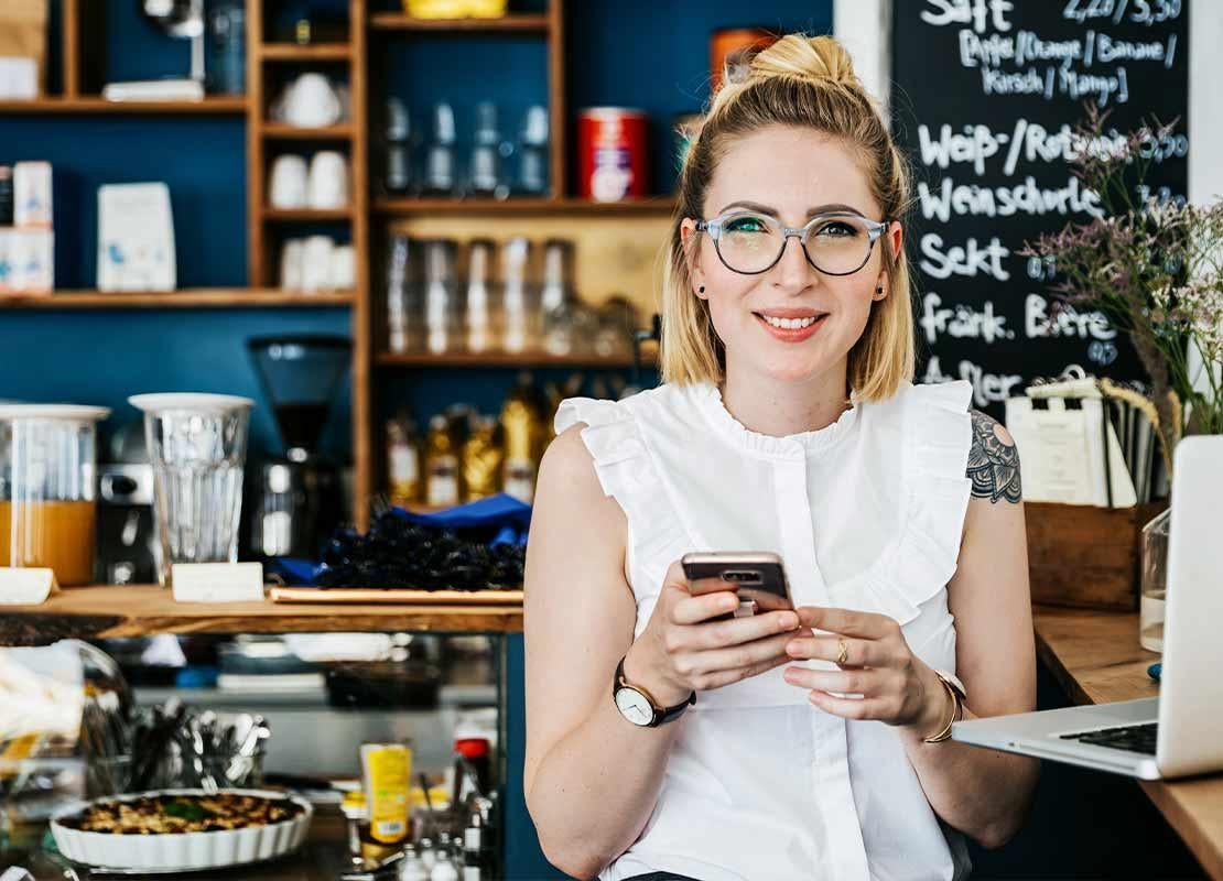 En zona de pago de una cafetería, cajera frente a una computadora sostiene un celular
