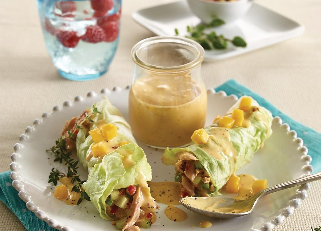 Plato con rollos primavera envueltos en lechuga y un recipiente con salsa, al fondo agua saborizada