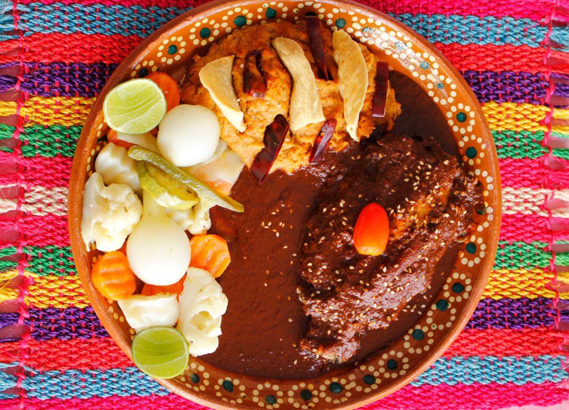 Platillo tradicional mexicano con carne en salsa, verduras y acompañamientos sobre mantel colorido.