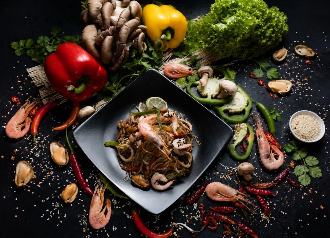 Plato con fideos, camarones y vegetales rodeado de ingredientes frescos