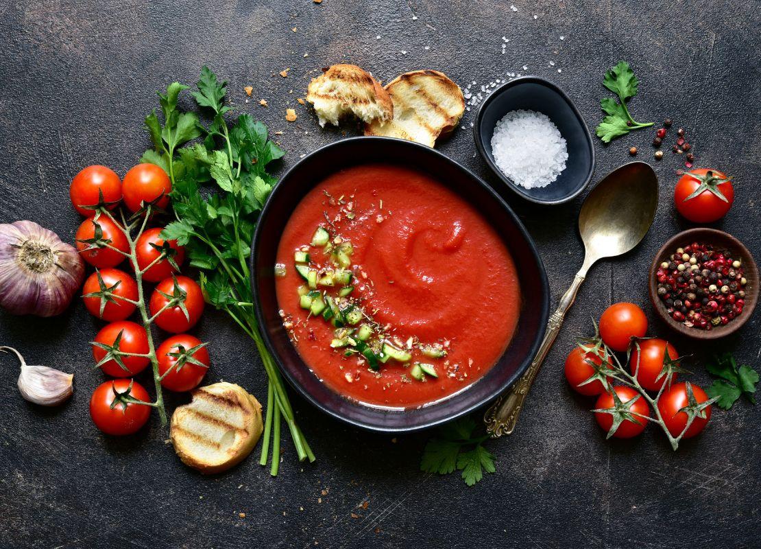 Plato con sopa de tomate acompañado de pan, hierbas y tomates