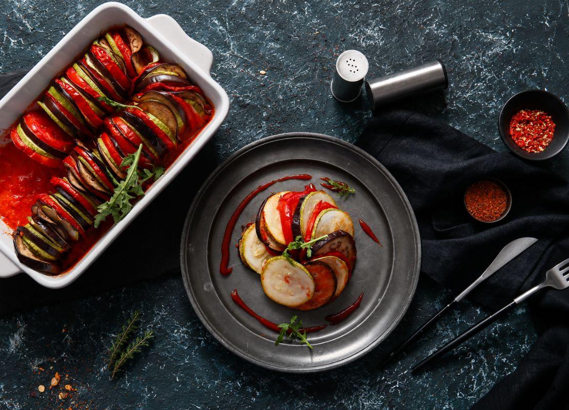 Rodajas de verduras horneadas que conforman un ratatouille en salsa servido en un plato y bandeja