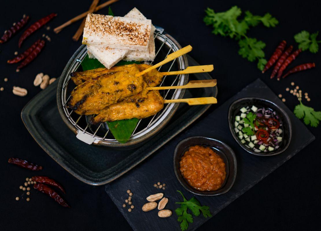 Brochetas de carne satay y uli bakar servidos con salsas y acompañamientos