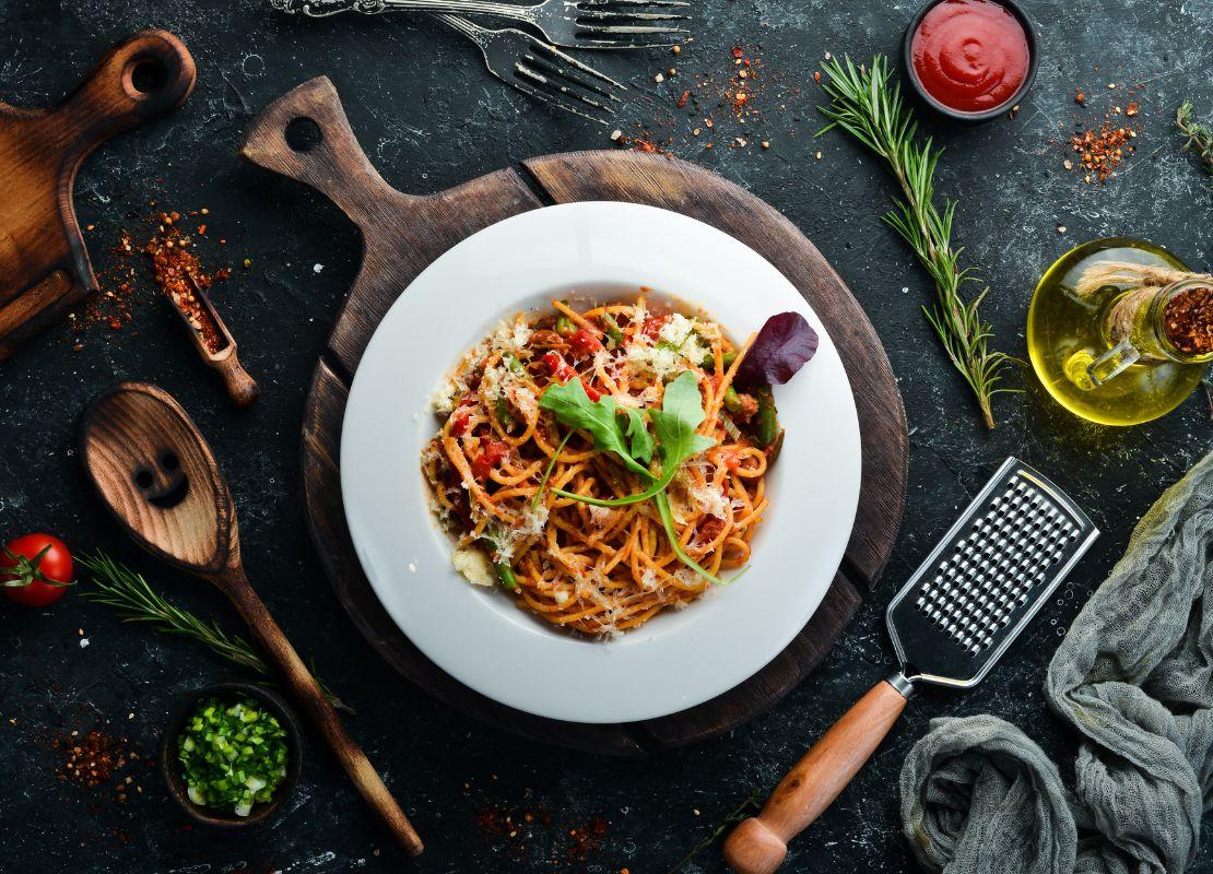 Plato de pasta con salsa, hierbas y queso servido en mesa con utensilios