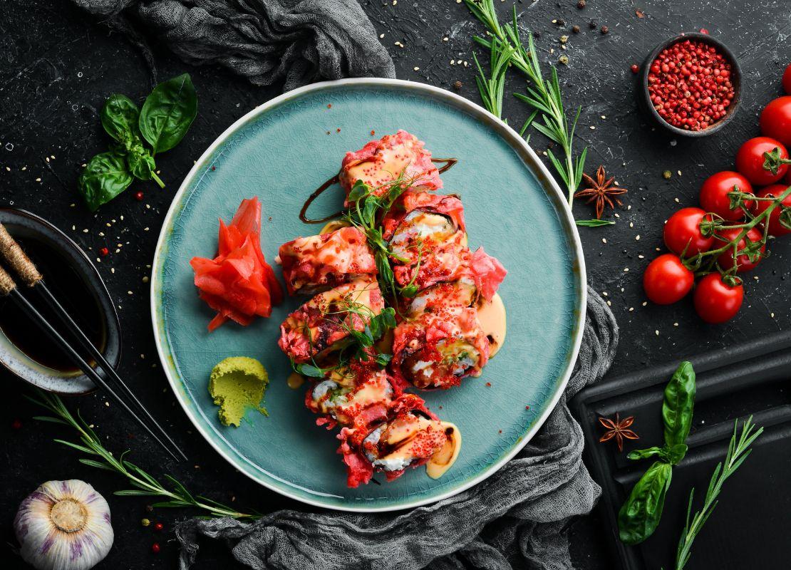 Piezas de sushi decoradas con salsa y hierbas en plato y rodeada de ingredientes frescos