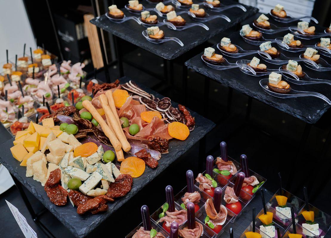 Tabla de quesos y embutidos junto a aperitivos individuales variados servidos en un catering.