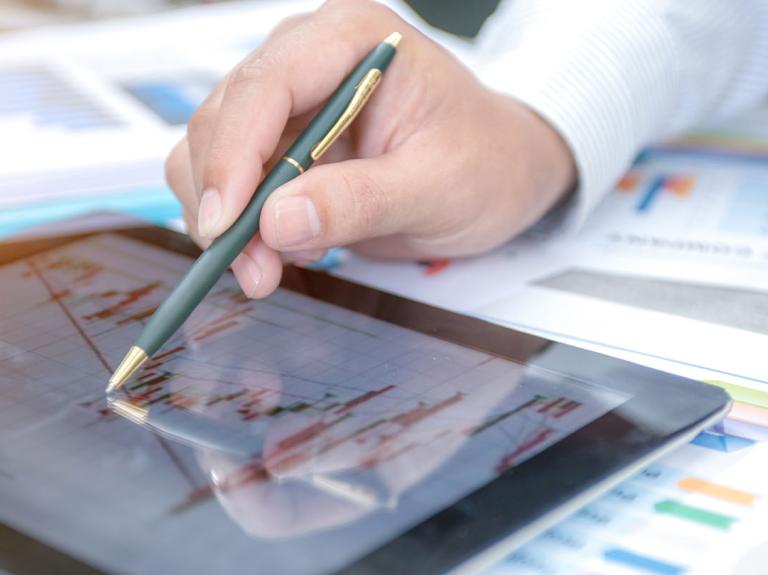 Mano con lapicero sobre una tablet con información sobre los costos fijos y variables
