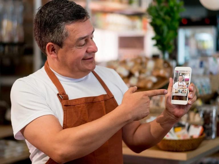 Barista en su negocio muestra en un smartphone el video creado para potenciar su plan de marketing gastronómico