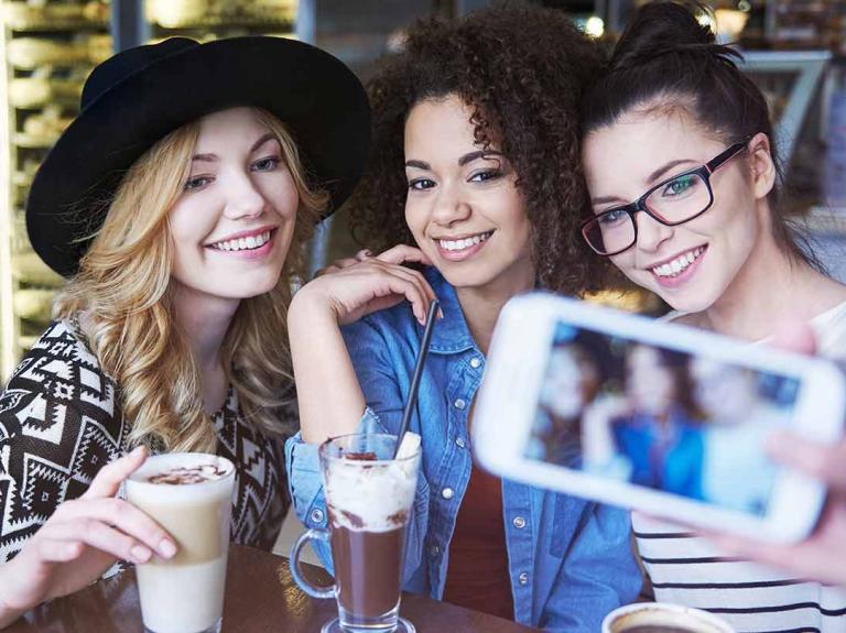 Tres influencers gastronómicas en una cafetería se toman fotos para crear contenido mientras disfrutan de diversas bebidas