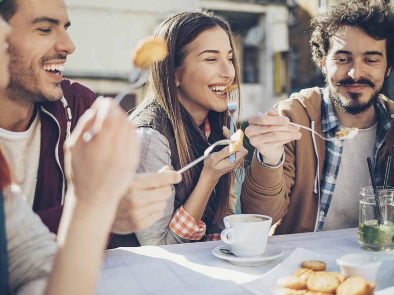Cinco comensales emocionados disfrutan al aire libre algunos bocadillos y bebidas en la mesa de un restaurante