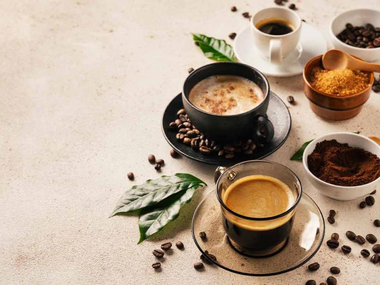 3 diferentes bebidas y productos de café junto con hojas y granos en una mesa
