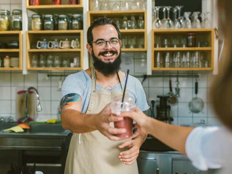 Barista entrega un smoothie, una de las bebidas para cafetería, a una clienta