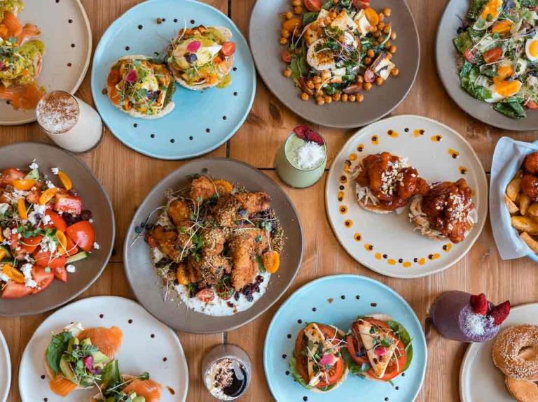 Varios platos que son parte de un menú de desayuno con huevos, vegetales y proteínas sobre una mesa