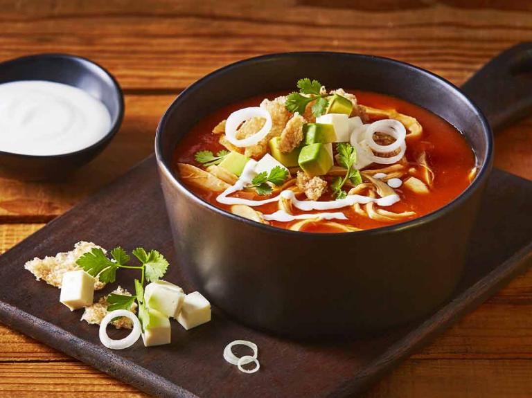 Sopa de pollo con verduras servida sobre una tabla y acompañada con crema de leche