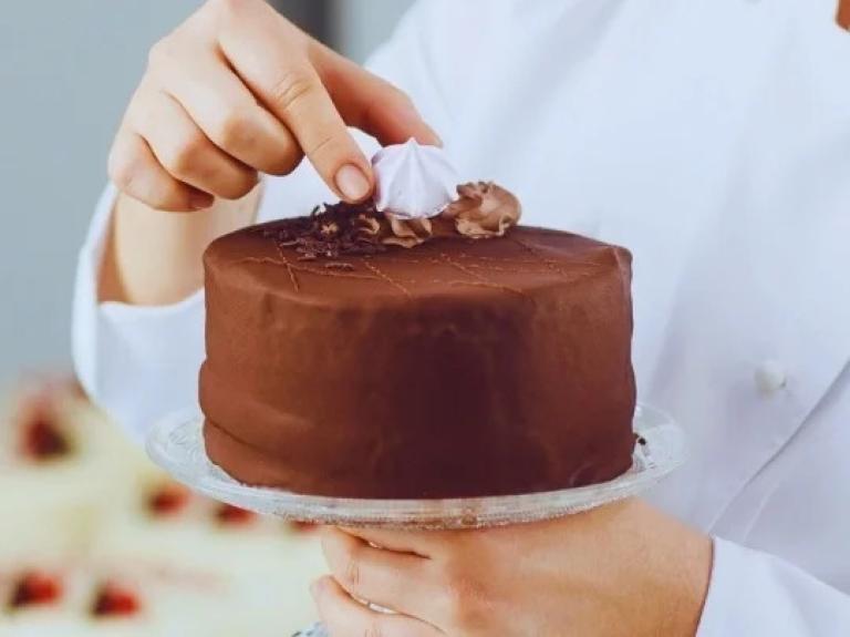 Persona con bata blanca sosteniendo un pastel de chocolate hecho con los insumos culinarios para negocios de Nestlé.