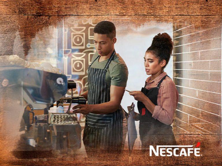 Un barista y un experto NESCAFÉ® con delantales preparando café en una cafetera profesional NESCAFÉ®.
