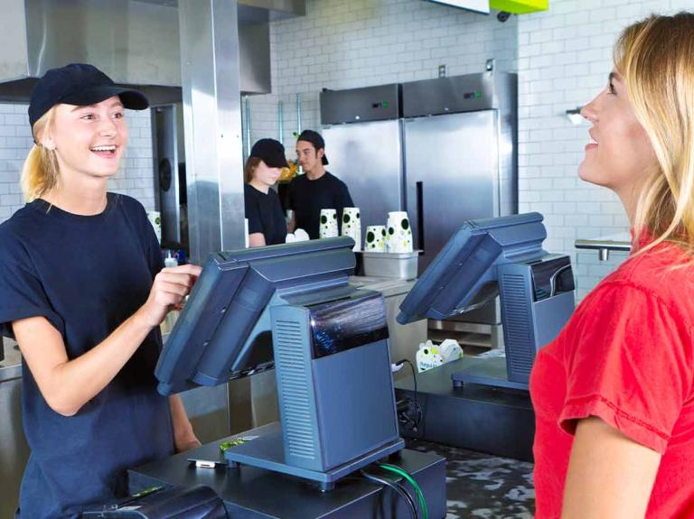 Una mujer arma la comanda de un restaurante atendiendo a otra mujer con dos trabajadores al fondo