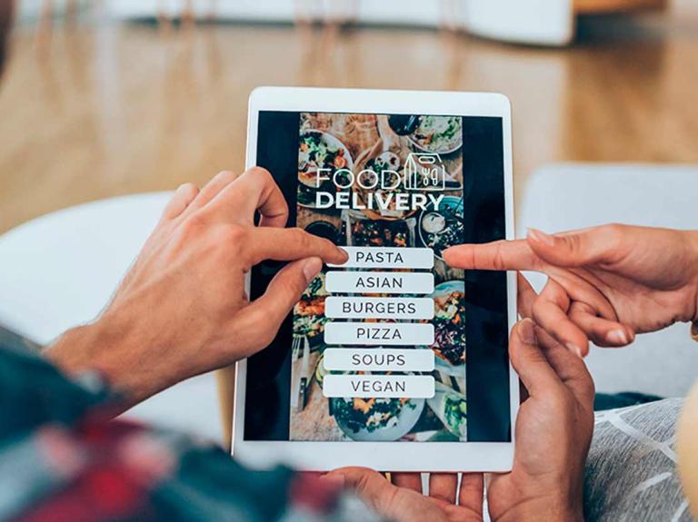 Manos de hombre y mujer sostienen una tablet en la que se muestra el menú digital de un restaurante