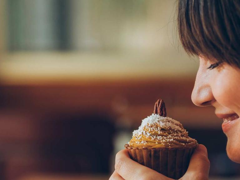 Mujer sostiene frente a su rostro un cupcake de frutos secos mientras disfruta su aroma