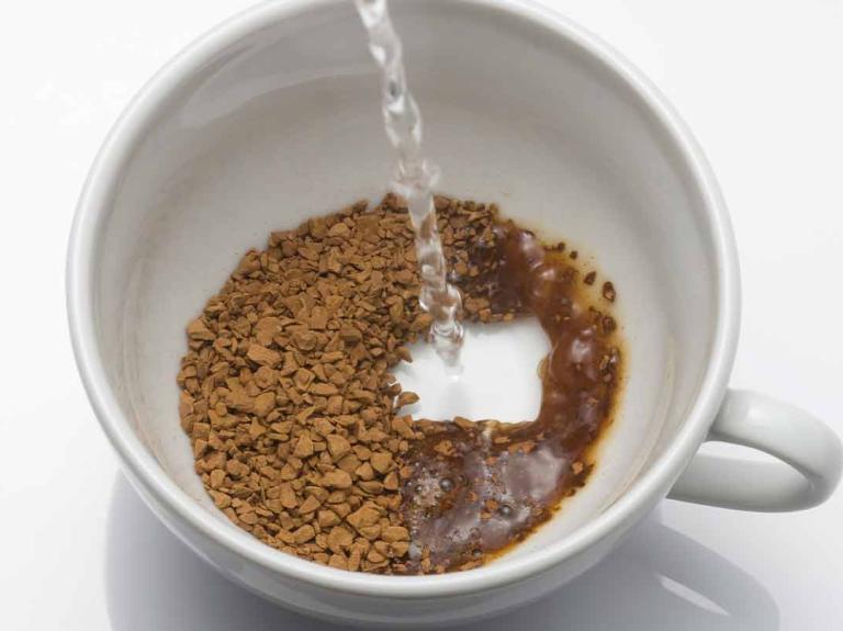 Taza de porcelana blanca con café soluble sobre el que se vierte agua caliente para preparar la bebida