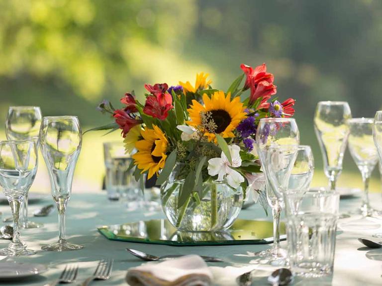 Mesa redonda al aire libre puesta para una comida formal con copas de cristal y flores en el centro