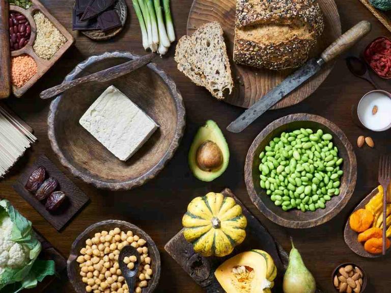 Diversos alimentos en recipientes de madera como frutas, verduras, tofu, frutos secos, cereales, entre otros