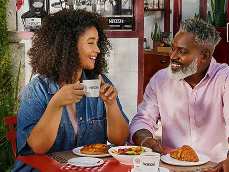 Un hombre y una mujer disfrutan del café NESCAFÉ® y desayuno al aire libre en una terraza