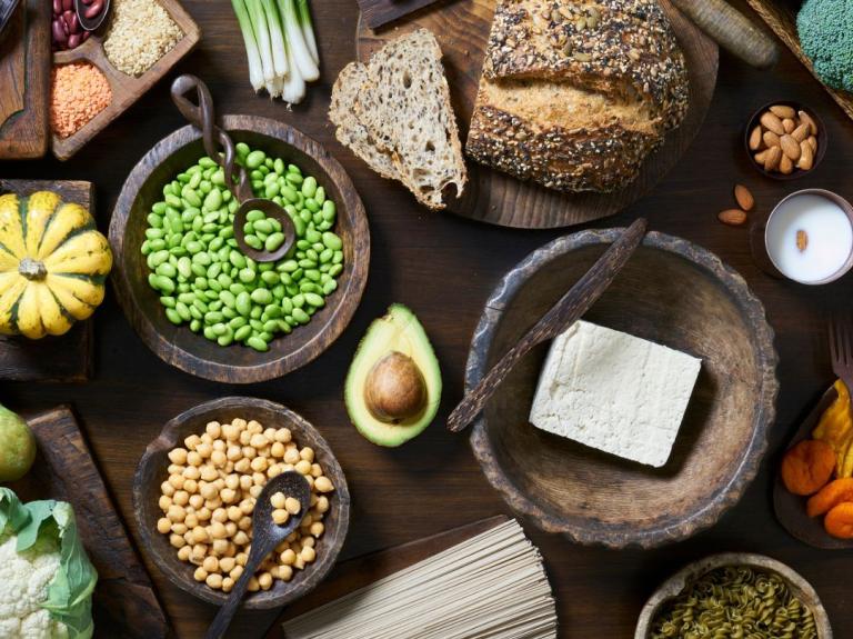Variedad de alimentos vegetales como tofu, legumbres, frutos secos y harinas integrales sobre una mesa rústica