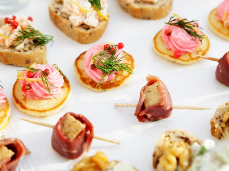 Variedad de canapés decorados con crema, eneldo, frutos rojos y carnes frías, dispuestos sobre una bandeja