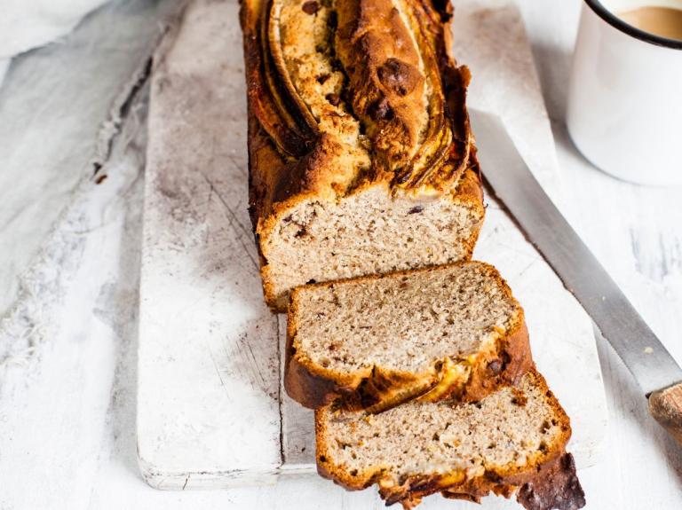 Pan de banano cortado en rebanadas, acompañado de una taza de café sobre fondo claro
