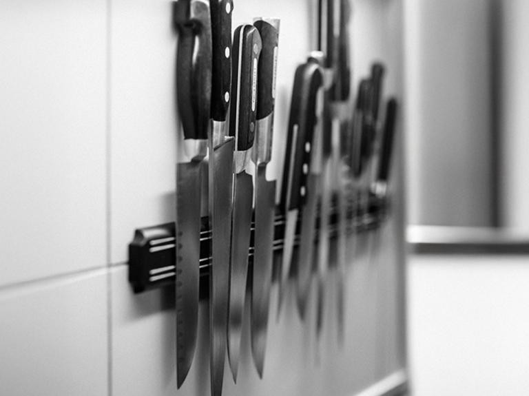 Varios cuchillos de cocina profesionales organizados sobre un soporte magnético en una pared blanca.
