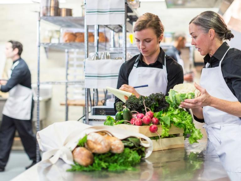 Dos chefs organizan ingredientes frescos, representando prácticas de cocina ecológica en un entorno profesional