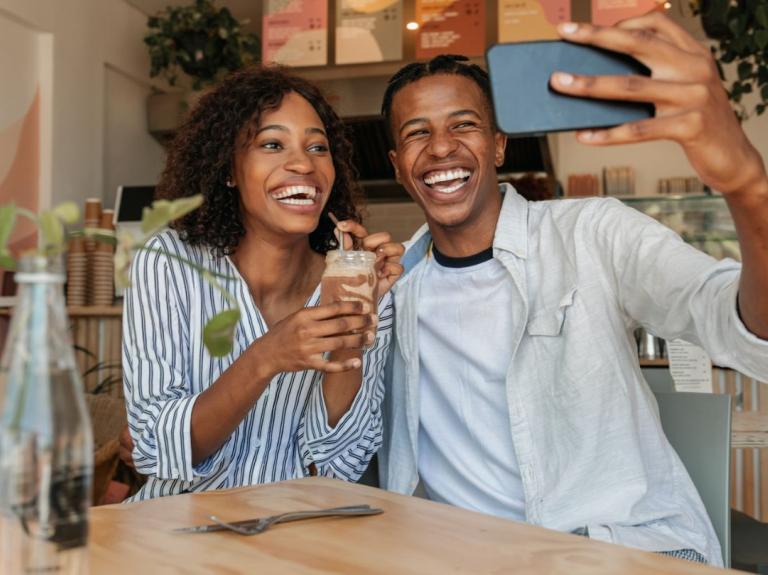 Una pareja sonriente se toma una selfie mientras disfruta una bebida en una cafetería moderna.