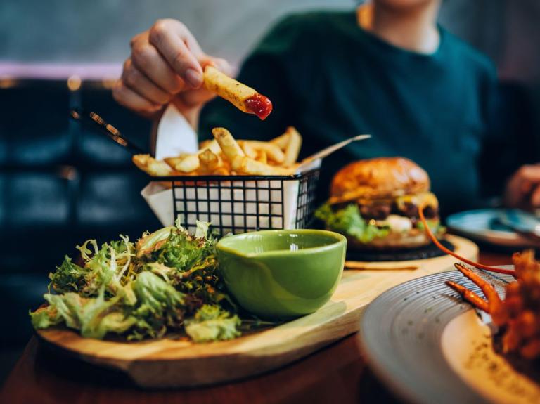 Persona disfrutando un menú casual con papas fritas, ensalada y hamburguesa en un restaurante.