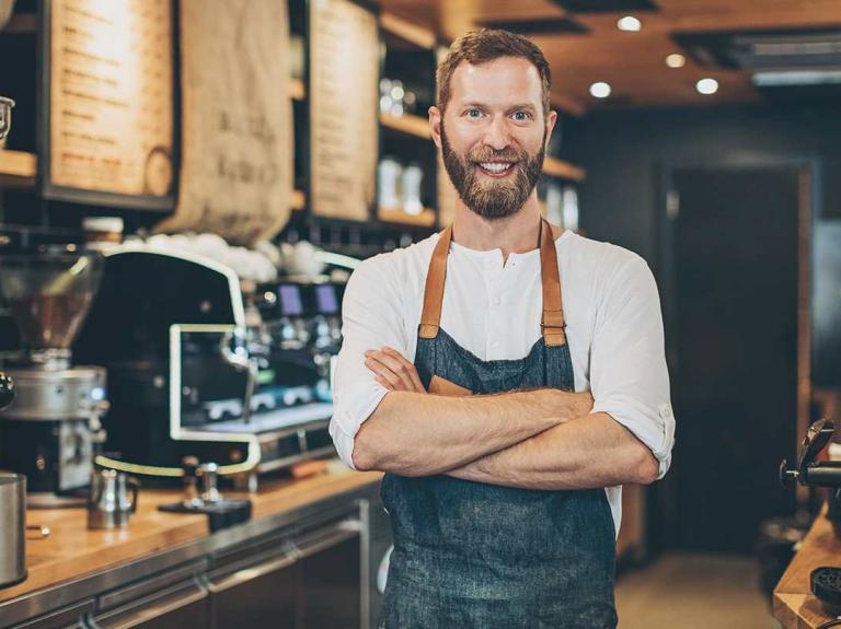 Barista sonriendo con los brazos cruzados tras el mostrador de en una cafetería