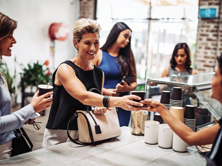 Personas reciben vasos desechables de café en un mostrador de una tienda de conveniencia