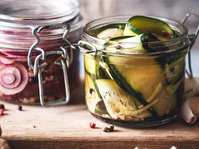 Dos frascos de cristal con cebolla y pepino fermentado sobre una tabla rodeada de ajos