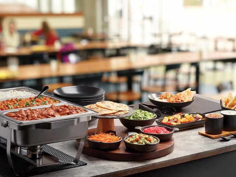Una food station con diferentes platos, guarniciones y salsas donde los comensales pueden sirvir su comida.