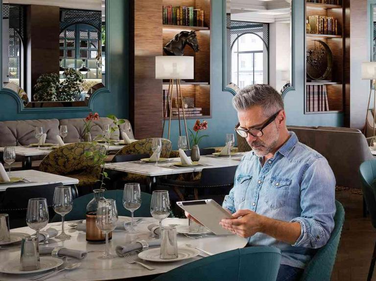 Persona revisa información en tablet dentro de un restaurante para hacer un comparativo de precios.