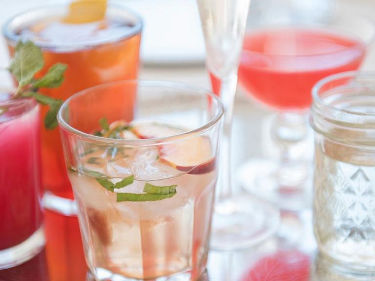 Bandeja con bebidas coloridas, servidas en vasos de cristal distintos estilos y decoradas con hielo, frutas y hierbas