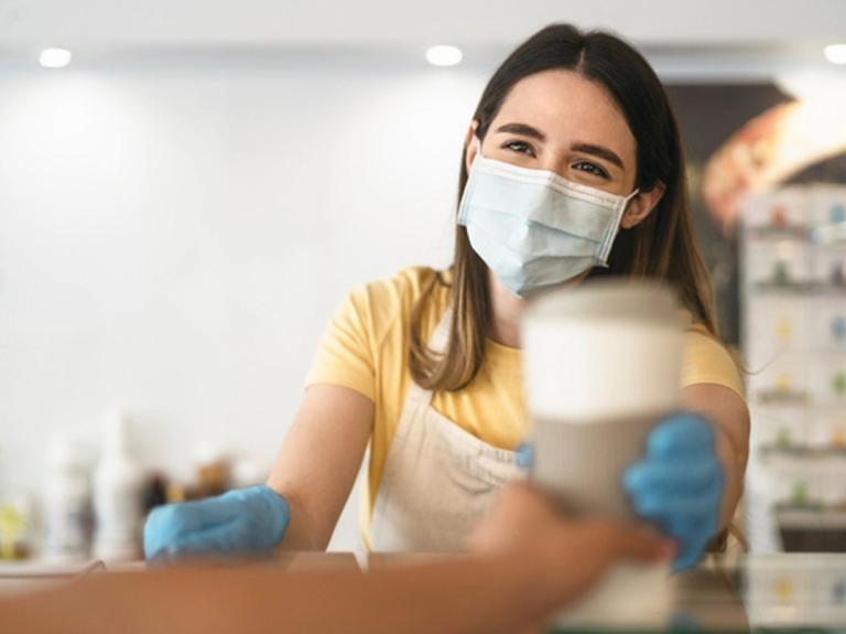 Trabajadora con mascarilla entrega una bebida como parte del servicio de alimentos en hospitales.