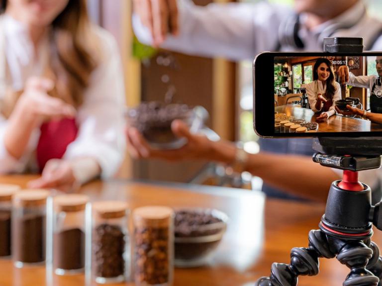 Blogger gastronómico graba contenido sobre café mostrando granos y preparación para redes sociales.