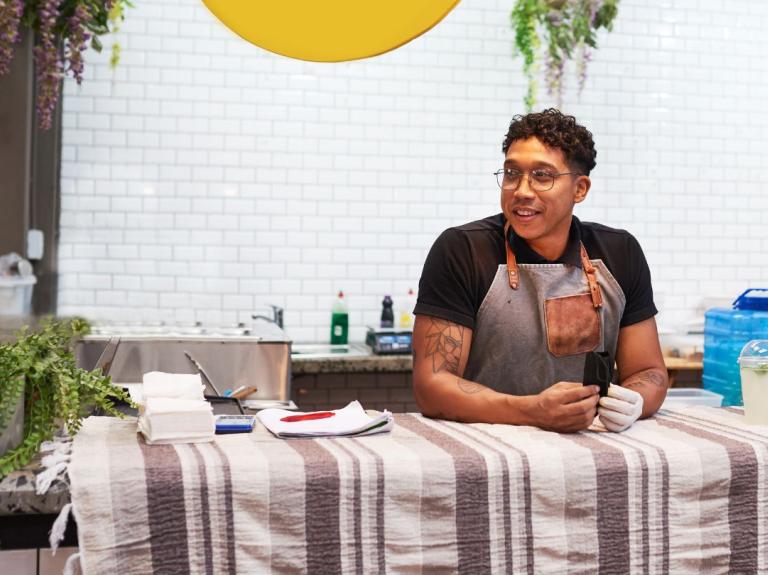 Hombre con delantal apoyado en mostrador de cocina con utensilios y plantas