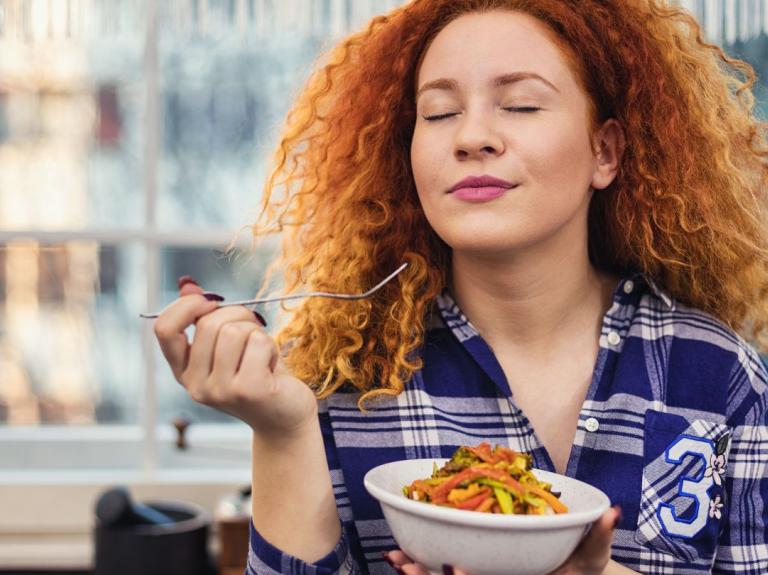 Mujer sostiene un bowl de comida y prueba con un tenedor con los ojos cerrados
