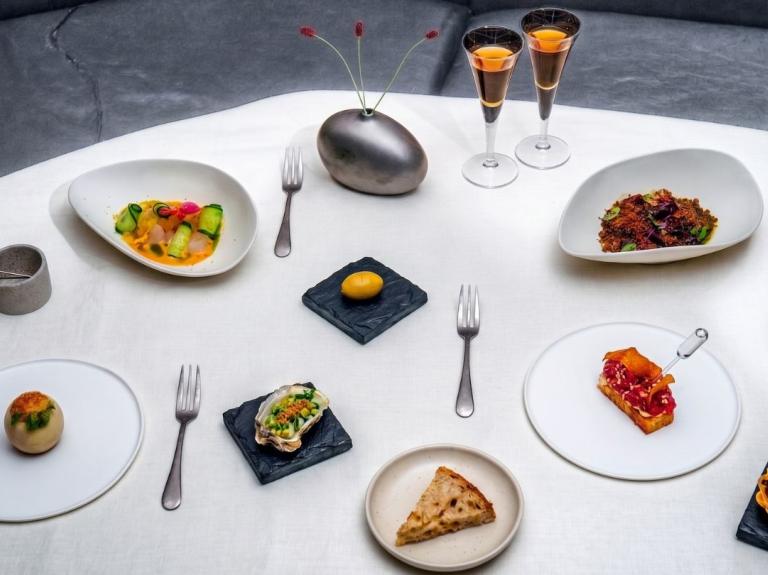 Varios platillos gourmet servidos sobre una mesa con mantel blanco y dos copas de vino fino.