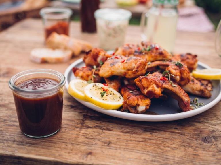 Alitas de pollo bañadas en salsa espesa tipo BBQ con brillo, presentadas en plato metálico